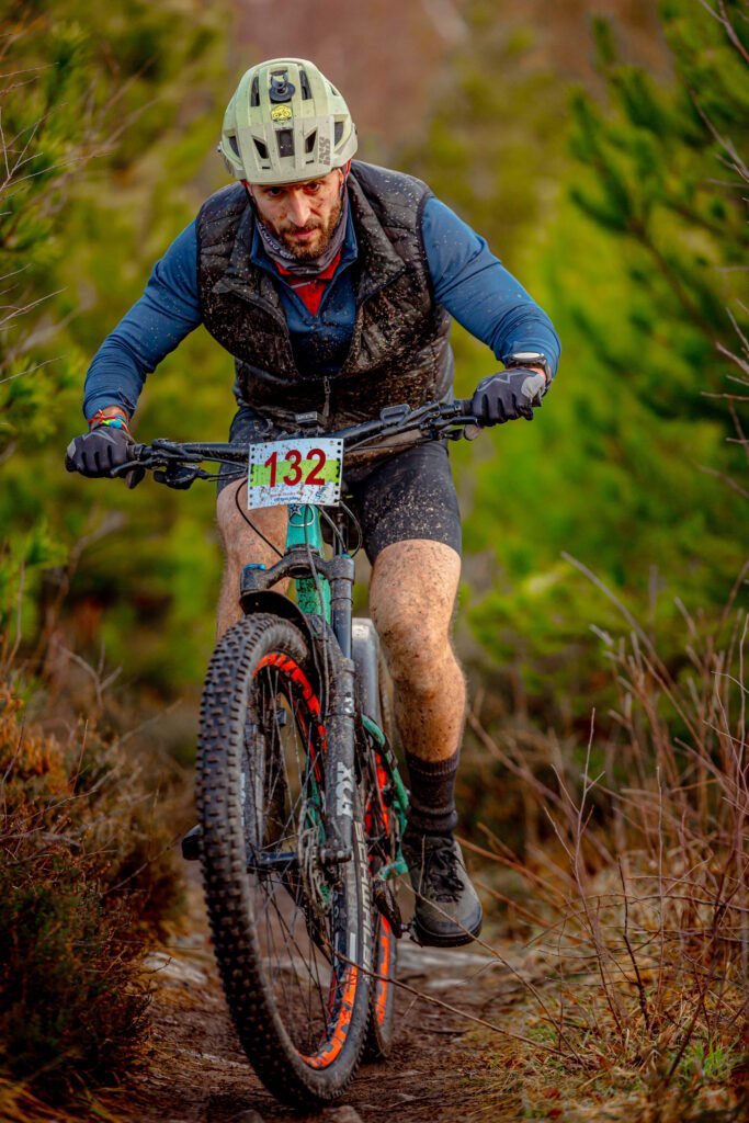 Roman riding his mountain bike during the Strathpuffer 2024, a 24-hour endurance race in Scotland, covered in mud and pushing through rugged terrain.