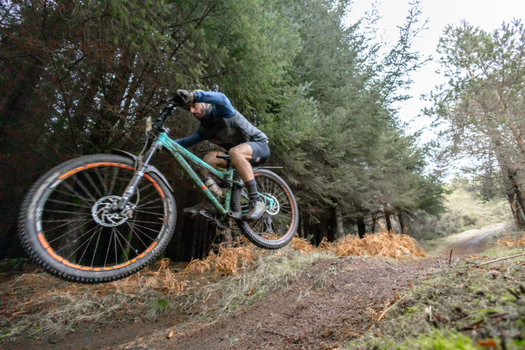 Roman riding his mountain bike during the Strathpuffer 2024, a 24-hour endurance race in Scotland, covered in mud and pushing through rugged terrain.